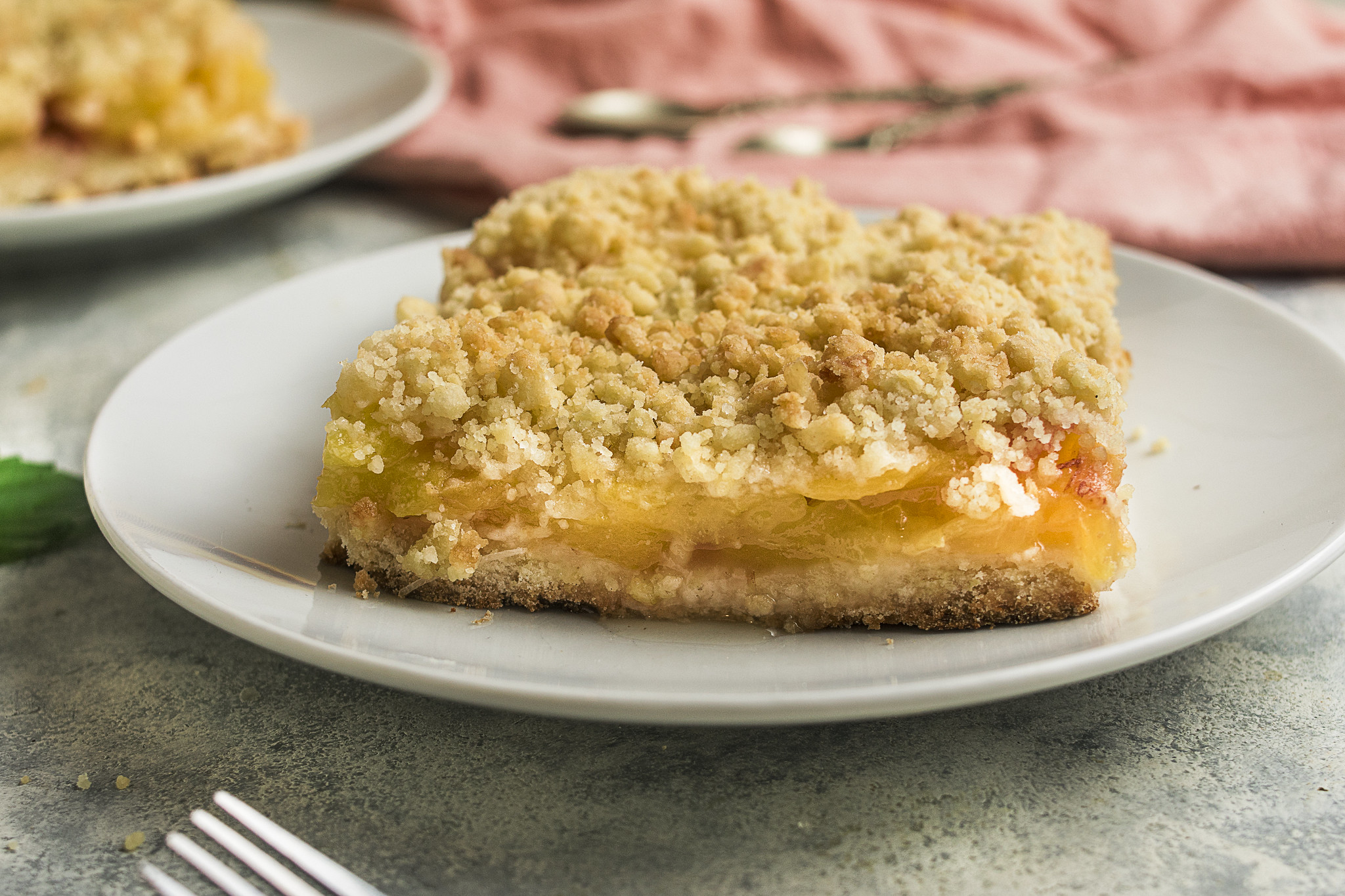 Close-up of sbriciolata di pesche on a white plate, showing the crumbly golden topping, juicy peach filling and buttery base.